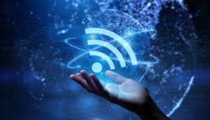 Hand holding a glowing Wi-Fi symbol surrounded by digital network elements on a blue background.