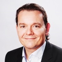Professional business portrait showing an individual wearing a formal suit jacket and collared shirt against a clean white background, representing corporate professionalism and an executive business profile.