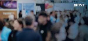 A wide shot of a busy indoor event or exhibition hall filled with many people moving and interacting. Booths, signage, and colorful displays are visible in the background, creating an active trade‑fair atmosphere. The ITVT logo appears in the upper‑right corner.