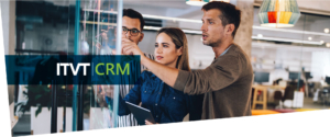 Drei Personen blicken auf ein Glasfenster mit der Aufschrift â€žITVT CRMâ€œ.