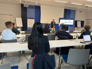 GeschÃ¤ftsprÃ¤sentation in einem Konferenzraum mit sitzenden Teilnehmern und einem Vortragenden, der an einem Podium spricht