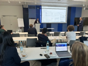 GeschÃ¤ftsprÃ¤sentation in einem Konferenzraum mit sitzenden Teilnehmern und einem Vortragenden, der an einem Podium spricht