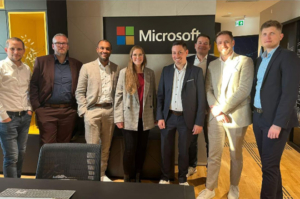 Eine Gruppe von Menschen, die vor einem Microsoft-Logo in einer BÃ¼roumgebung stehen und lÃ¤cheln.