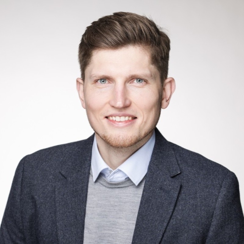 Professionelles PortrÃ¤tfoto einer Person, die einen dunklen Blazer, ein hellblaues Hemd und einen grauen Pullover trÃ¤gt, verwendet fÃ¼r ITVT-Unternehmensmaterialien.