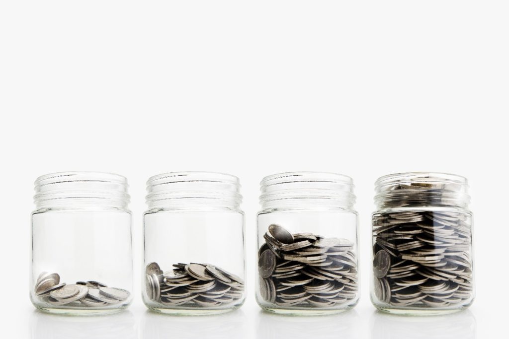 Vier transparente Glasgefäße, die in einer Reihe angeordnet sind und jeweils immer mehr Münzen enthalten, symbolisieren das strukturierte Wachstum, die Investitionsstrategie und den nachhaltigen Unternehmenswert von ITVT.